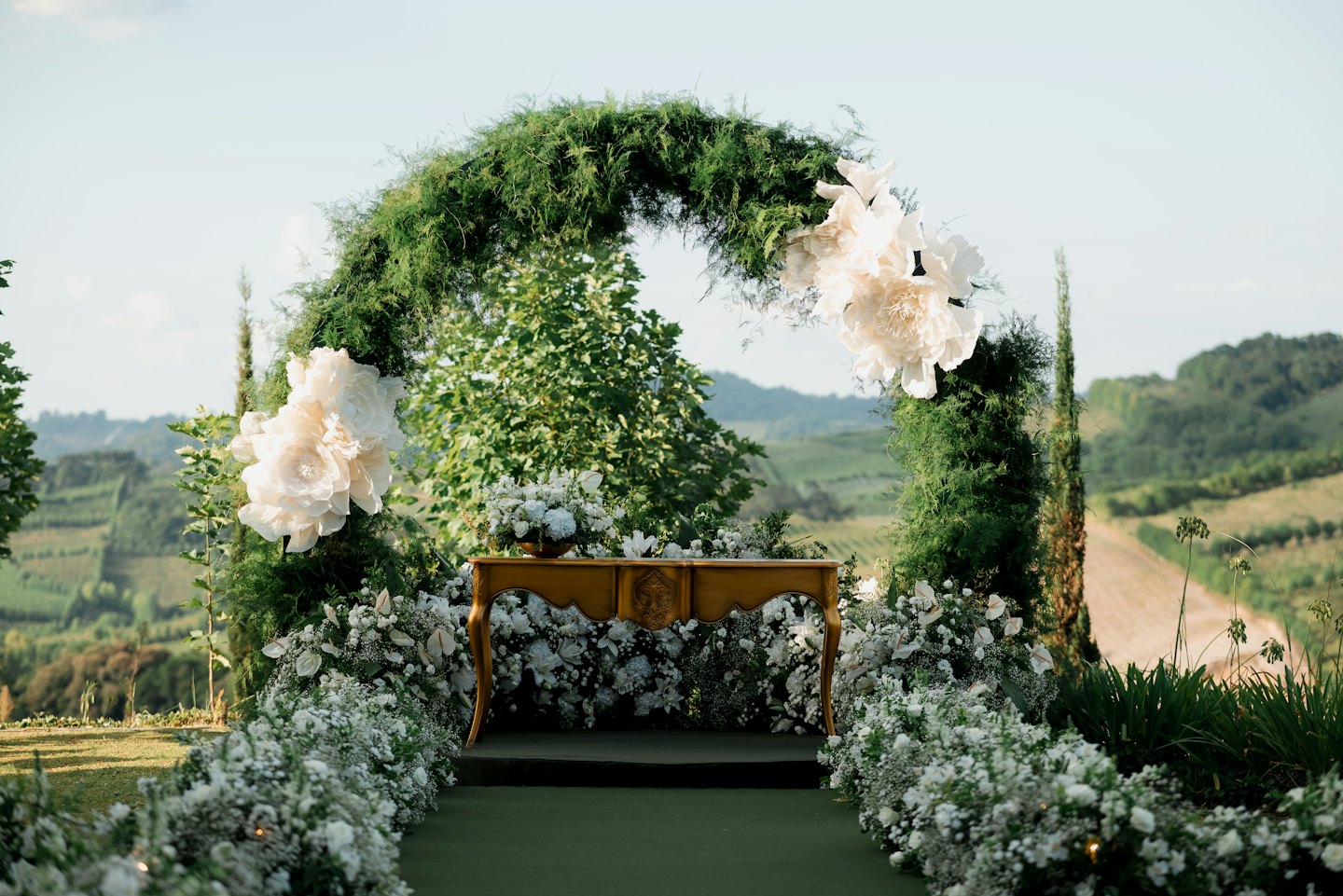 Outdoor wedding arch with white paper flowers on a lawn.